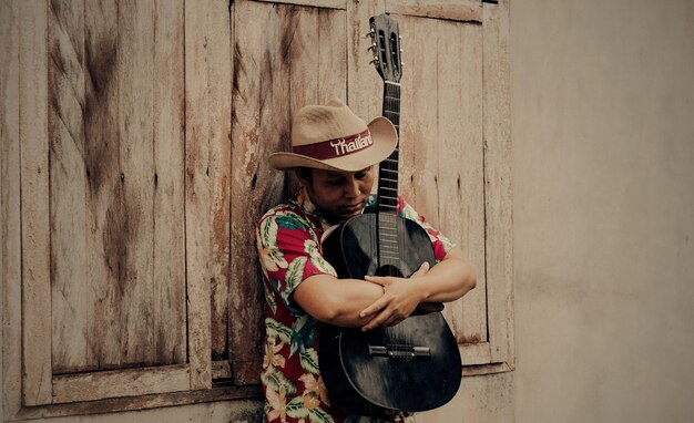 Foto homem maduro segurando uma guitarra enquanto está de pé junto à parede