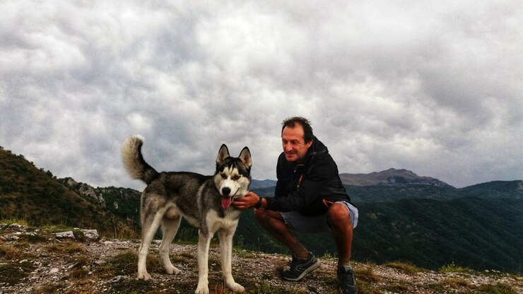 Foto homem maduro sorridente mimando cão no pico da montanha contra o céu nublado