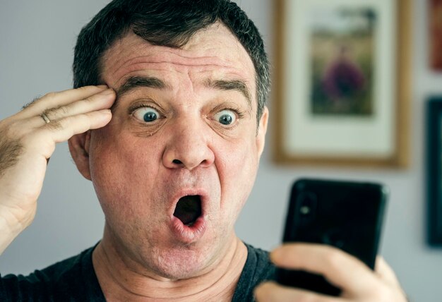 Homem maduro surpreso usa um rosto de close-up de smartphone
