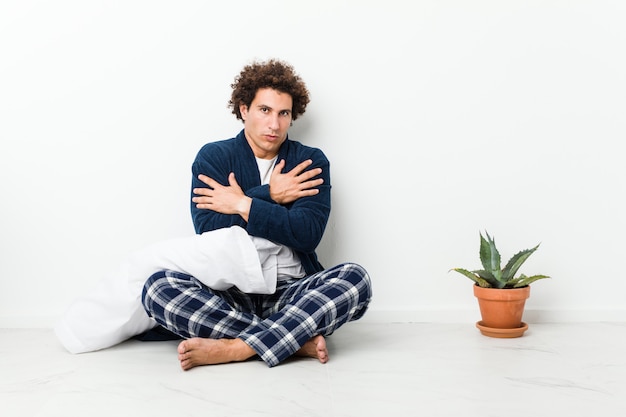 Homem maduro, vestindo pijama, sentada no chão da casa, esfriando devido à baixa temperatura ou uma doença.