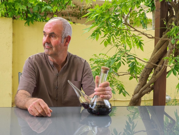 Homem mais velho sentado em uma mesa com um copo de vinho tinto na mão