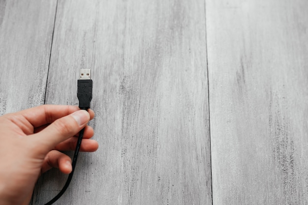 Homem mantém um tipo de usb um cabos em fundo branco de madeira