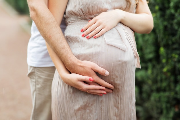 Homem mãos abraço mulher grávida por barriga closeup. ficar linda gravidez menina vestida de vestido.