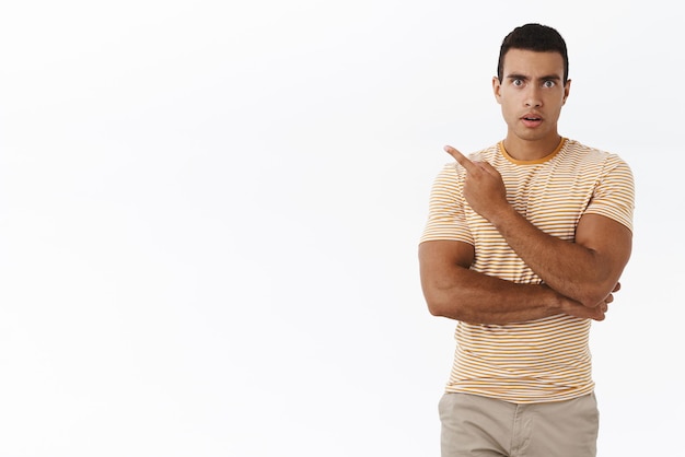 Foto homem masculino caucasiano confuso e intrigado, perguntando sobre o produto no espaço em branco vazio, apontando o dedo no fundo esquerdo.