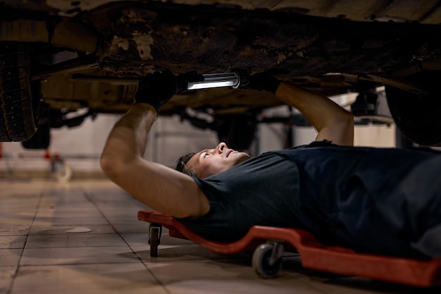 Homem mecânico de automóveis experiente trabalhando sozinho no chão reparando a parte inferior do carro, observe os detalhes...