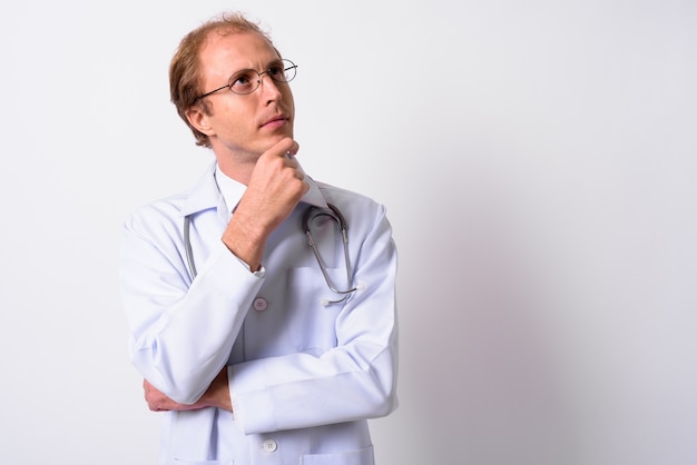 homem médico com cabelo loiro e óculos contra uma parede branca