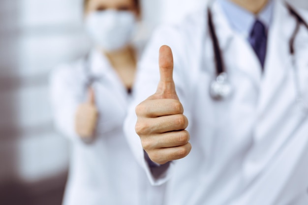 Homem-médico desconhecido e mulher em linha reta como uma equipe e mostrando sinal de Ok com polegares para cima na clínica moderna. Conceito de medicina durante a pandemia de Coronavirus. Covid 2019.