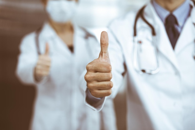 Homem-médico desconhecido e mulher em pé como uma equipe e mostrando sinal de Ok com polegares para cima na clínica moderna. Conceito de medicina.