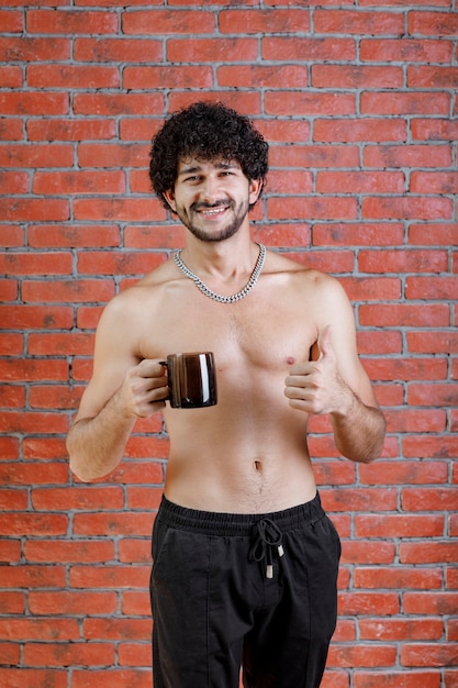 Homem meio nu de cabelo encaracolado segurando uma xícara de chá.