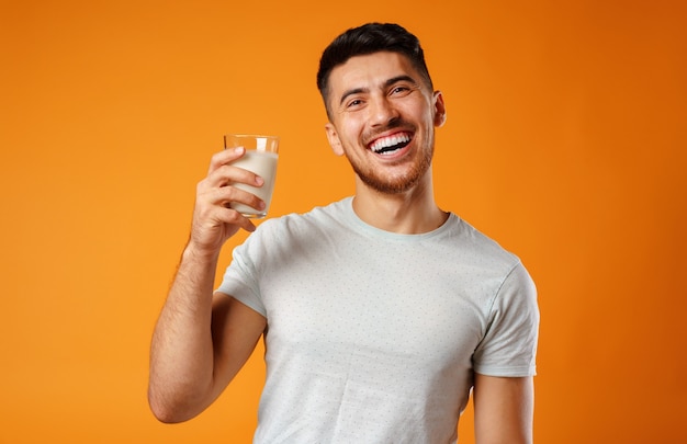 Homem mestiço sorridente feliz segurando leite contra amarelo close-up