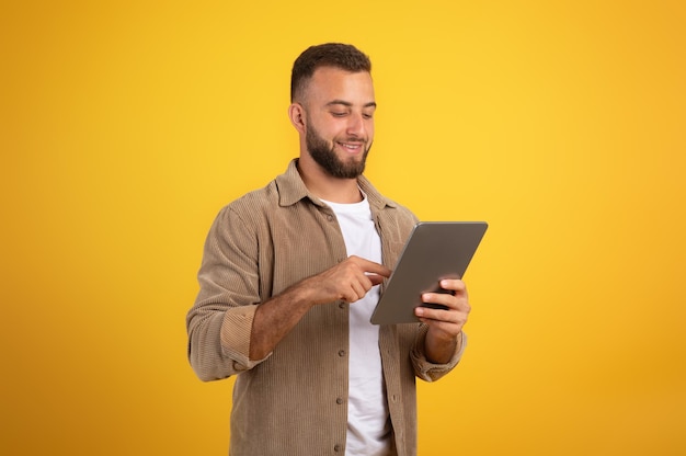 Homem milenar europeu atraente, confiante e positivo, com barba, usa tela sensível ao toque do tablet