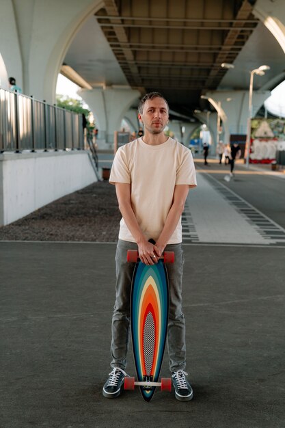 Homem milenar segura skate ou longboard dentro de casa em um espaço urbano para treinos radicais de patinação