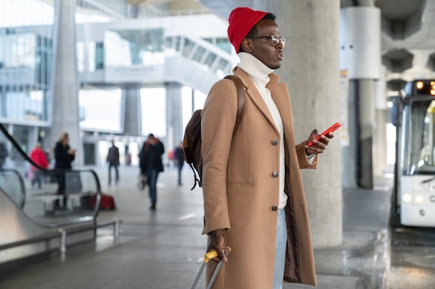 Homem milenar viajante afro-americano com mala segurando o celular