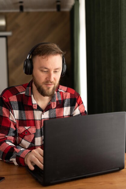 Foto homem millennial caucasiano feliz trabalhando em laptop com fones de ouvido enquanto está sentado no local de trabalho em escritório moderno negócios e empreendedorismo carreira de sucesso e trabalho remoto
