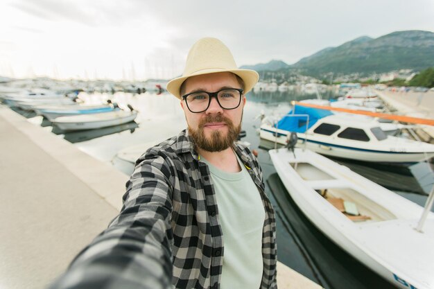 Homem millennial viajante tirando selfie de iates de luxo marinho durante a viagem de dia ensolarado e verão