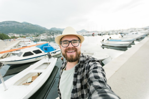 Homem millennial viajante tirando selfie de iates de luxo marinho durante a viagem de dia ensolarado e verão