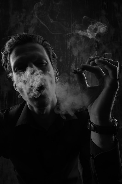 Homem misterioso com charuto e fumaça isolado no fundo preto.