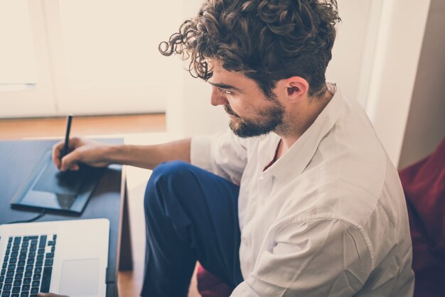 Foto homem moderno bonito hipster trabalhando em casa usando o laptop