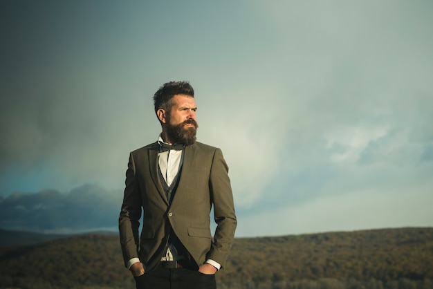 Homem moderno com barba e bigode no rosto com a barba por fazer. homem de negócios da moda usa um casaco clássico com gravata borboleta.