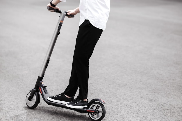 Homem moderno com roupa elegante preto e branco, andar de scooter elétrica na cidade.