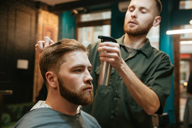 homem moderno cortando cabelo de cabeleireiro enquanto está sentado na cadeira.