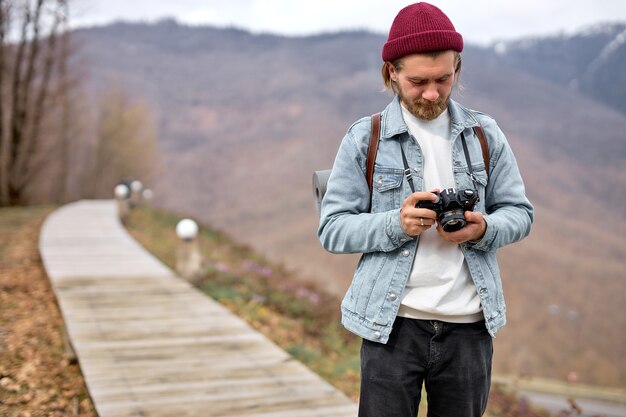 Homem moderno do fotógrafo, caminhadas e vagando. Conceito de viagens e aventura. Cara bonito tirando foto na câmera, na natureza, ao ar livre. copie o espaço. retrato do barbudo olhando para a tela da câmera