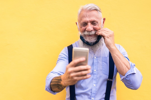 Homem moderno na moda, usando telefone celular, fazendo chamadas de vídeo enquanto usava máscara de segurança de seda da moda