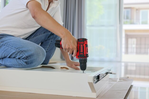 Homem montando móveis de mesa branca em casa usando chave de fenda sem fio