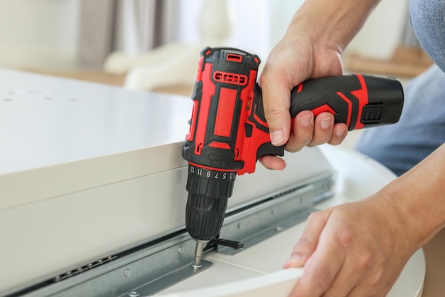 Homem montando móveis de mesa brancos em casa usando uma chave de fenda sem fio