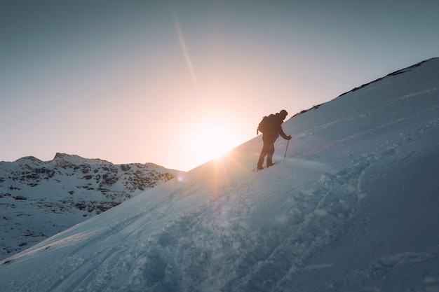 Homem montanhista com trekking pole climbing em colina nevada e sol no monte ryten, ilhas lofoten