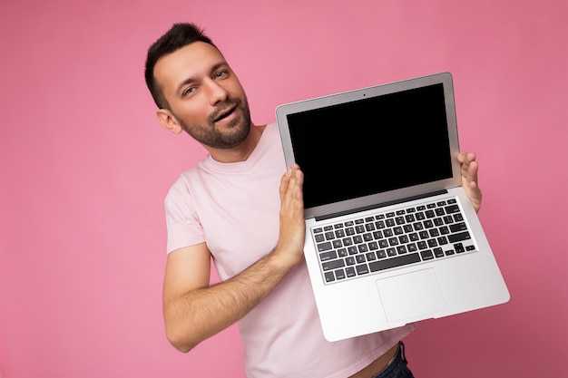 Homem moreno bonito segurando um laptop com um monitor preto em branco para maquete, olhando para a câmera