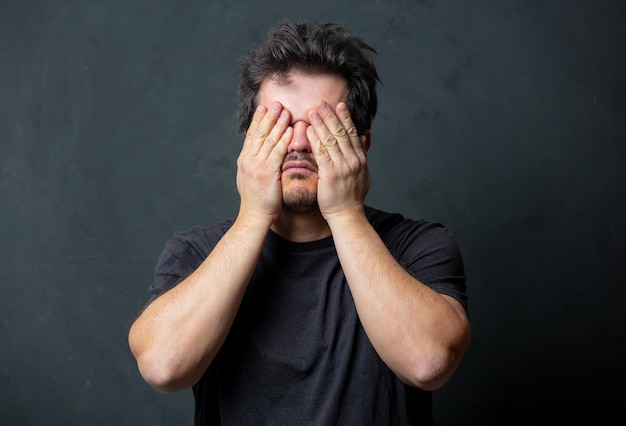 Homem moreno cansado de camiseta preta na parede escura