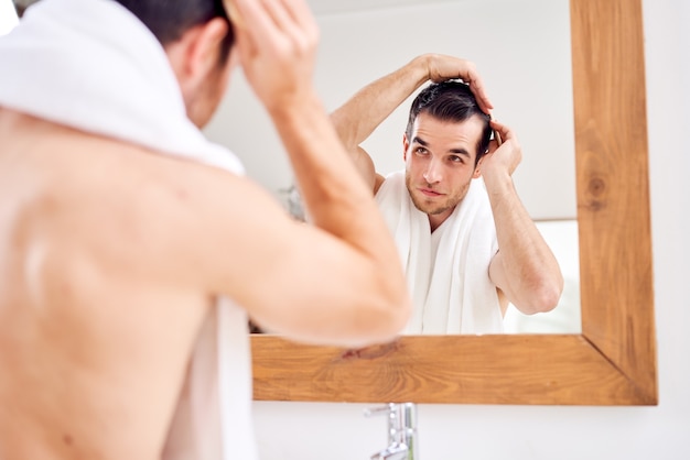 Homem moreno penteando o cabelo enquanto está no banheiro diante do espelho