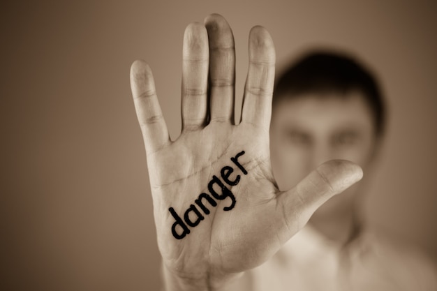 Homem mostrando a palavra "perigo" escrita na palma da mão