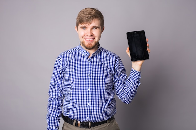 Homem mostrando a tela em branco do tablet na parede cinza.