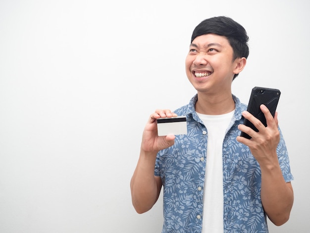 Homem mostrando cartão de crédito e celular muito feliz olhando para o espaço da cópia