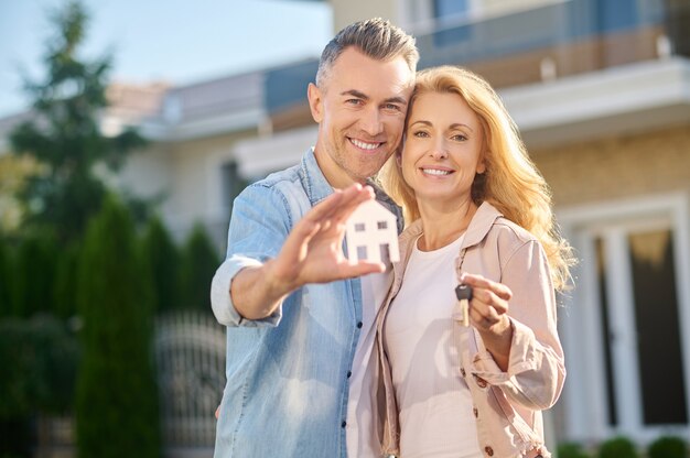 Homem mostrando sinal de casa e esposa com chave