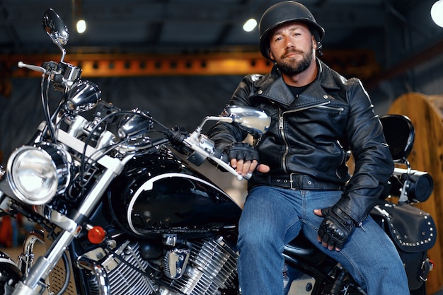 Homem motociclista de jaqueta de couro e capacete, sentado em sua motocicleta