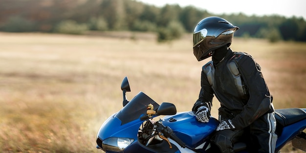 Homem motociclista em uma motocicleta com uma jaqueta de couro e capacete olha para a estrada