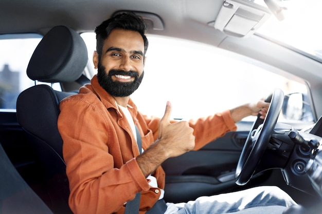 Homem motorista indiano feliz gesticulando polegares para cima dirigindo carro
