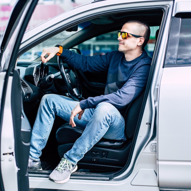 Homem motorista sorridente sentado no carro com a porta aberta. Homem adulto no veículo