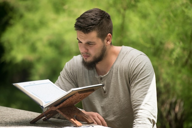 Foto homem muçulmano adulto está lendo o alcorão do lado de fora em um parque