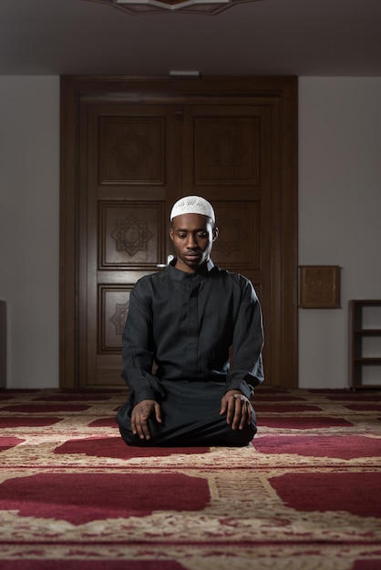 Homem muçulmano africano fazendo oração tradicional a Deus enquanto usava um boné tradicional Dishdasha