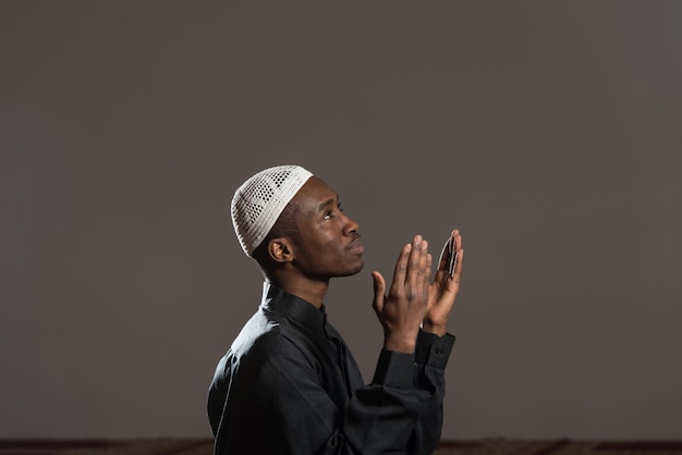 Homem muçulmano africano fazendo oração tradicional a Deus enquanto usava um boné tradicional Dishdasha