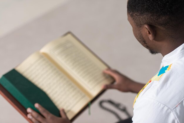 Homem muçulmano africano lendo livro islâmico sagrado Alcorão