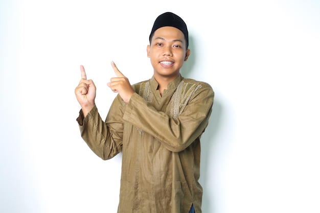 homem muçulmano asiático apontando para cima e sorrindo para a câmera usando vestido islâmico isolado no fundo branco