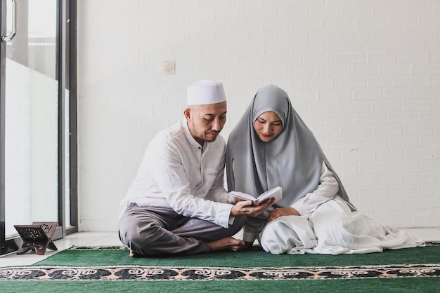 Homem muçulmano asiático ensinando sua esposa a ler o Alcorão durante o mês de Ramadã na mesquita