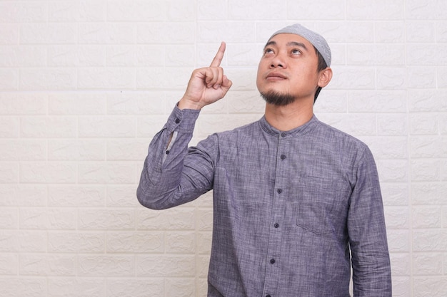 Foto homem muçulmano asiático religioso apontando dedos para cima louvor a deus pose sobre o fundo da parede branca