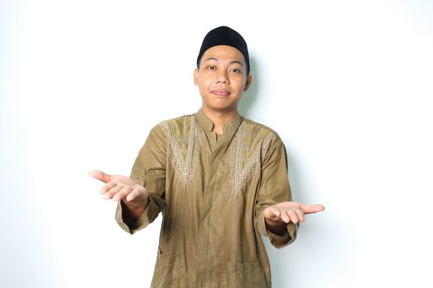 homem muçulmano asiático satisfeito vestindo roupas koko apresentando-se para a câmera com a palma da mão aberta, isolada no fundo branco