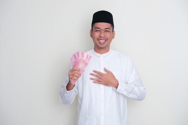 Homem muçulmano asiático segurando dinheiro com gesto grato
